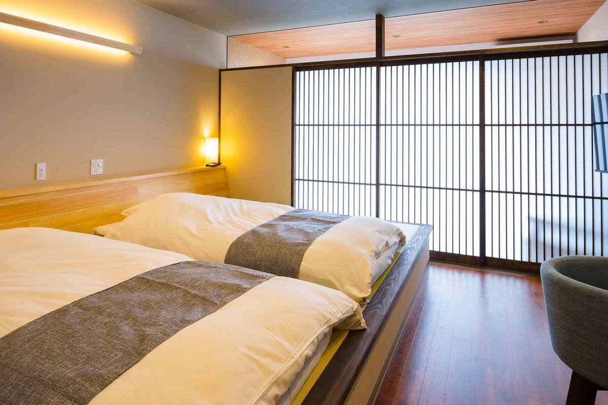 A hotel room with a bed, bedside lamps, a chair, and a view through a shoji screen.