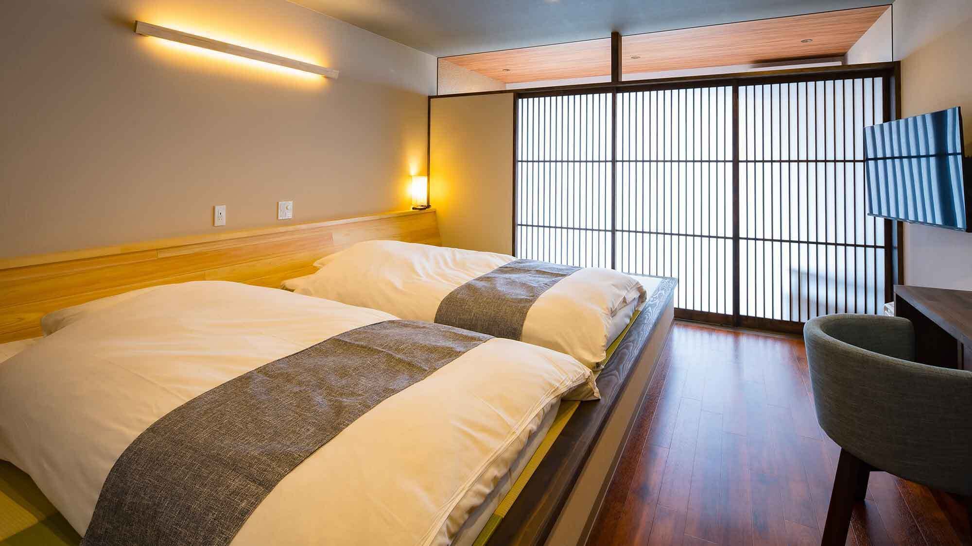 Ein Hotelzimmer mit Bett, Stuhl, Wandleuchte und einem großen Fenster mit vertikalen Jalousien.