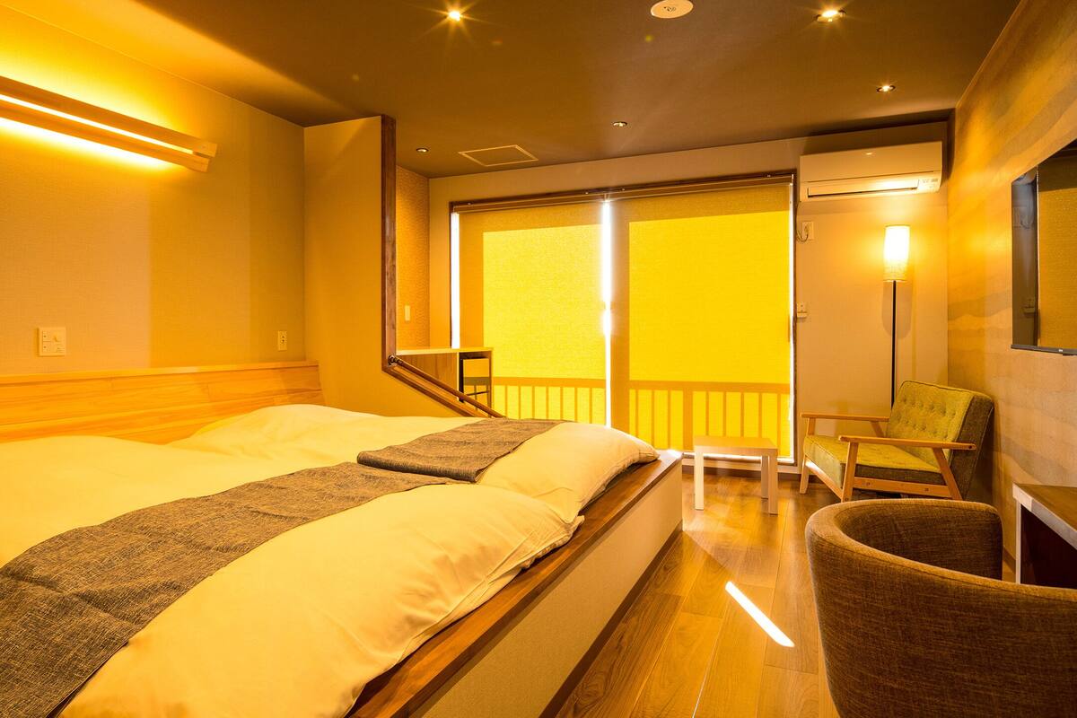 A hotel room with a bed, a chair, a desk, and a view of the outside.