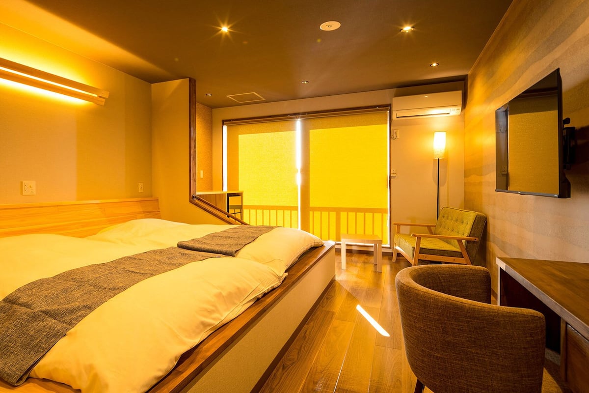 A hotel room with a bed, a chair, a desk, a balcony, and a view of the outside.