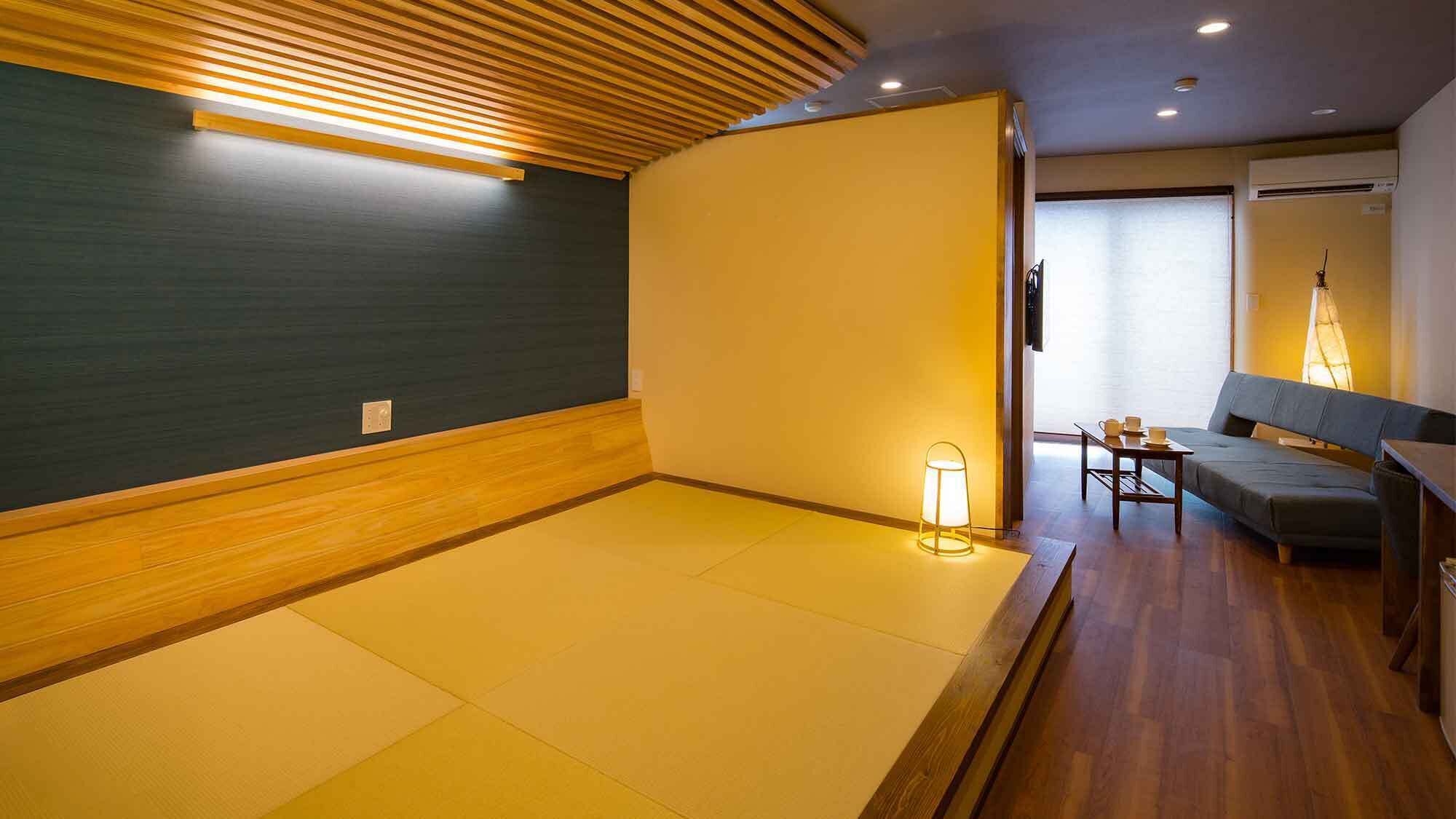 Ein Zimmer mit Tatami-Böden, einer Holzzahlendele und einer Couch, einem Tisch mit Tassen sowie einer Lampe.