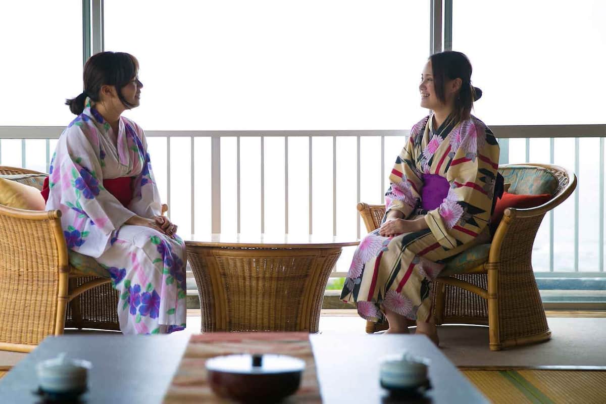 Deux personnes, vêtues de tenues traditionnelles, sont assises à une table devant laquelle se trouve un balcon.