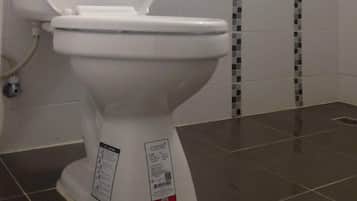 A bathroom with a white toilet, a shower with a tiled wall, and a shelf with toiletries.