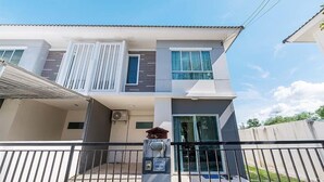 A modern two-story house with a balcony, a garage door, and a security gate.