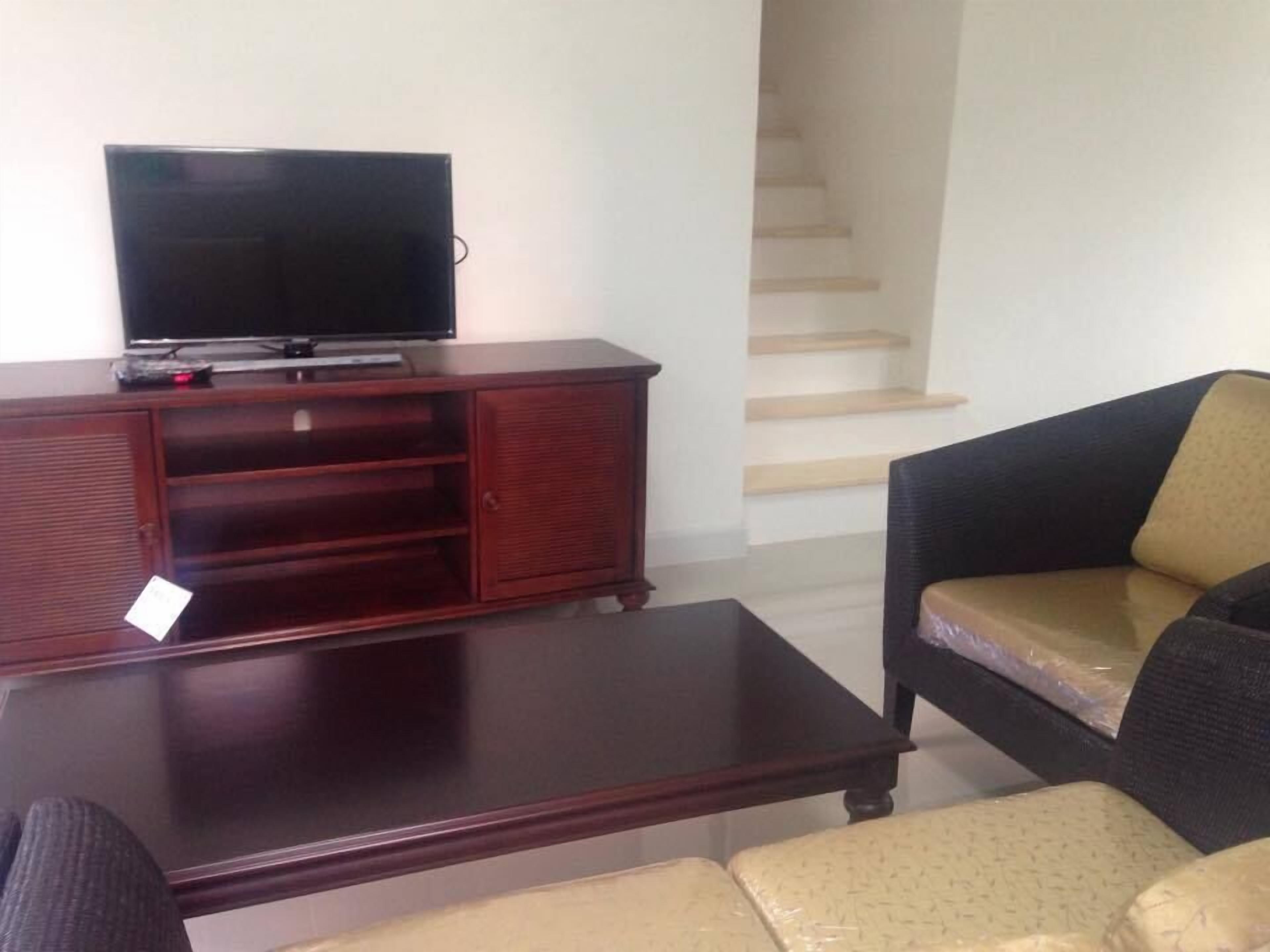 A living room with a dark wooden entertainment center, a flat-screen TV, a dark coffee table, and a black and beige sofa.