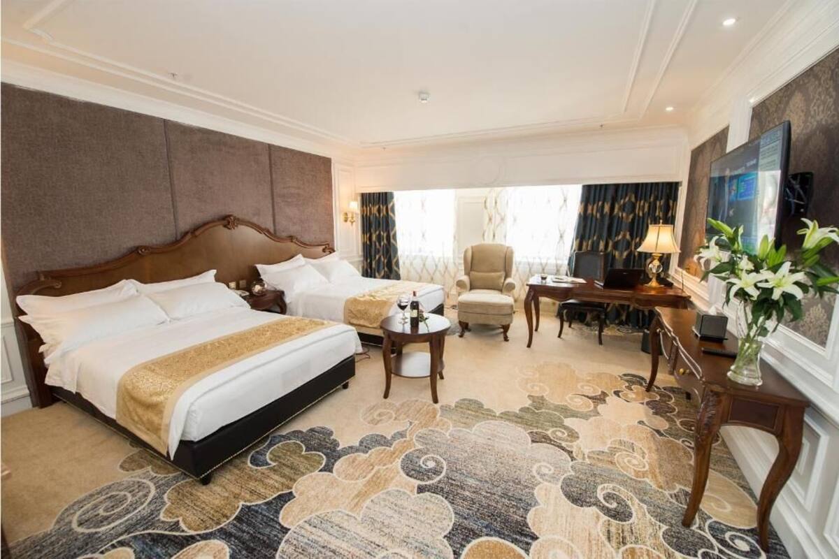 A hotel room with a large bed, a smaller bed, a desk, a chair, and a television.