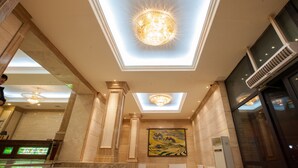 A hotel lobby with a large chandelier, a painting on the wall, and a large window.
