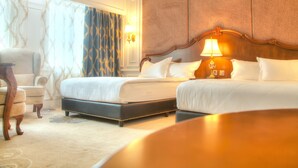 A hotel room with two beds, a sitting area, and a large window with curtains.