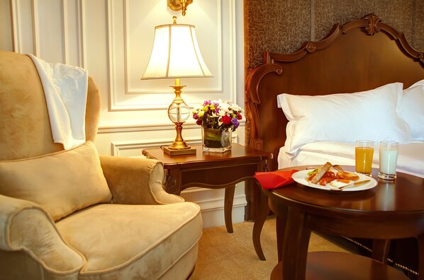 Una habitación de hotel con cama, mesita de noche con lámpara, un jarrón de flores y una bandeja de desayuno.
