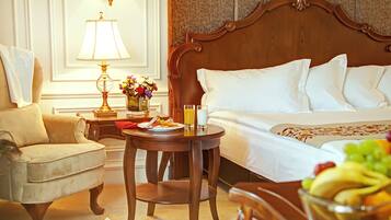 Una habitación de hotel con cama, una silla, una mesa con lámpara, un jarrón de flores y un frutero.