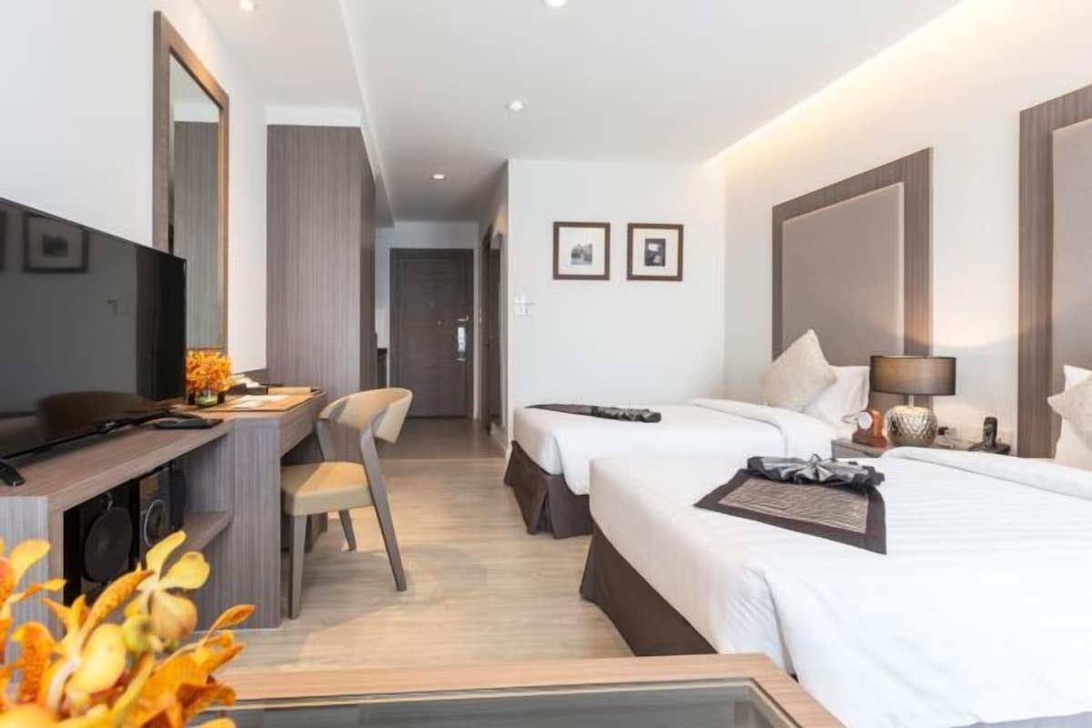 Habitación de hotel con escritorio, dos camas, televisor y espejo.