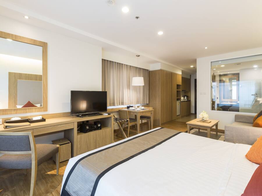 Habitación de hotel con cama, escritorio, silla, televisión y vista de la ciudad a través de un ventanal grande.