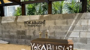 En receptionsdisk på Yokabushi Glamping Resort, med en bakgrund av en vägg klädd med sten och tropiska växter.