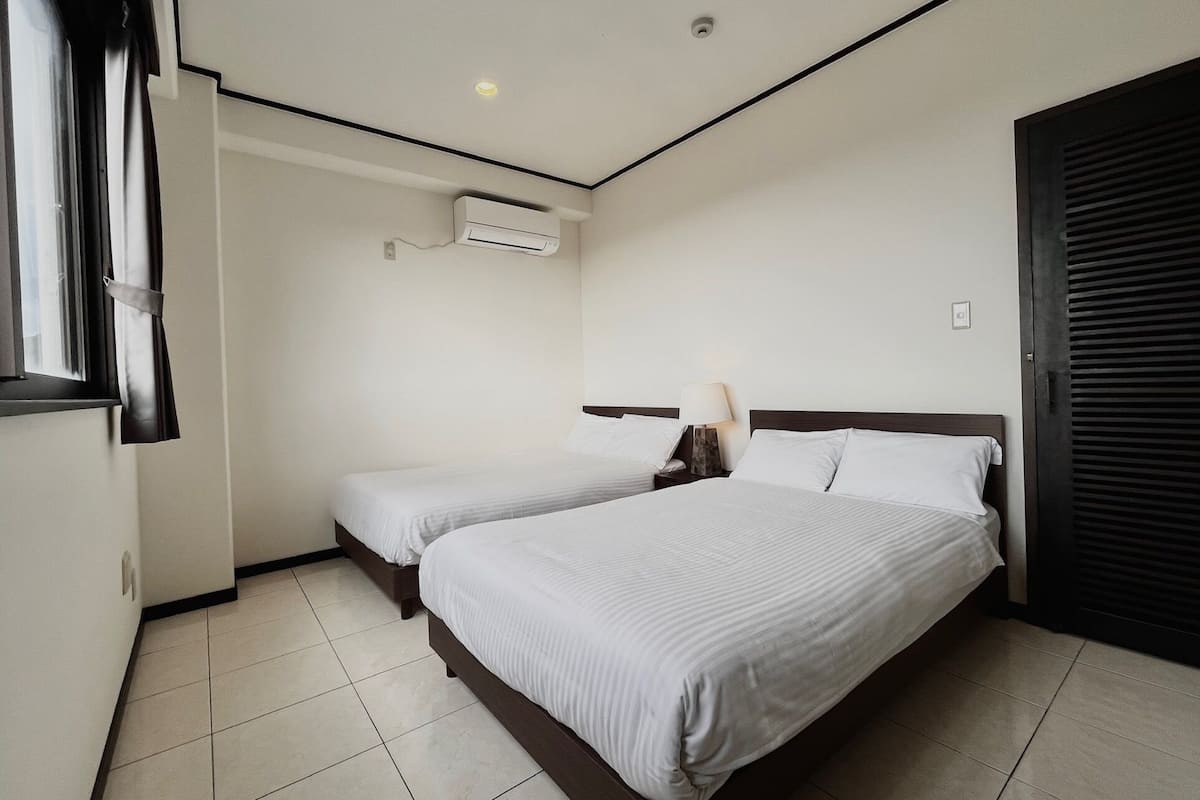 Une chambre d’hôtel avec deux lits, une fenêtre avec des rideaux, un appareil de climatisation et une porte avec un volet.