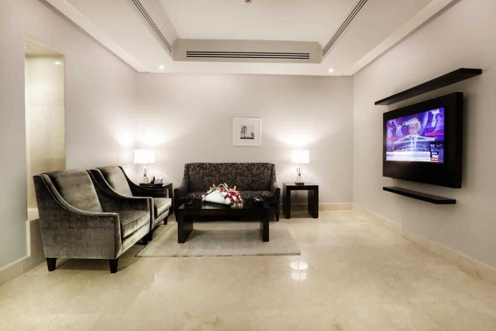 A modern living room with a sofa, two armchairs, a coffee table, and a flat-screen TV mounted on the wall.