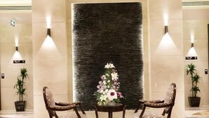 Un hall con una mesa redonda, dos sillas, un centro de mesa floral y una pared con textura.