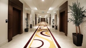 Un pasillo de hotel con una alfombra de diseño, puertas de madera y plantas en macetas.