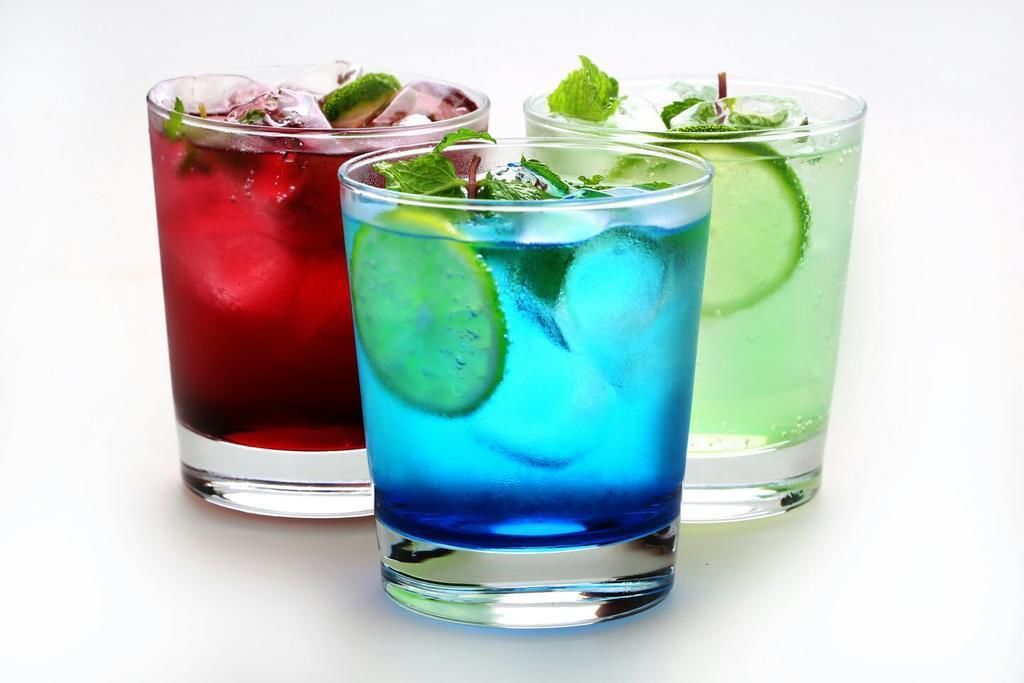 Three glasses of colorful beverages with mint leaves and ice cubes.