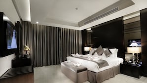 Una habitación de hotel moderna con una cama grande, un televisor de pantalla plana, una mesita de noche con lámpara y un ventanal con cortinas.