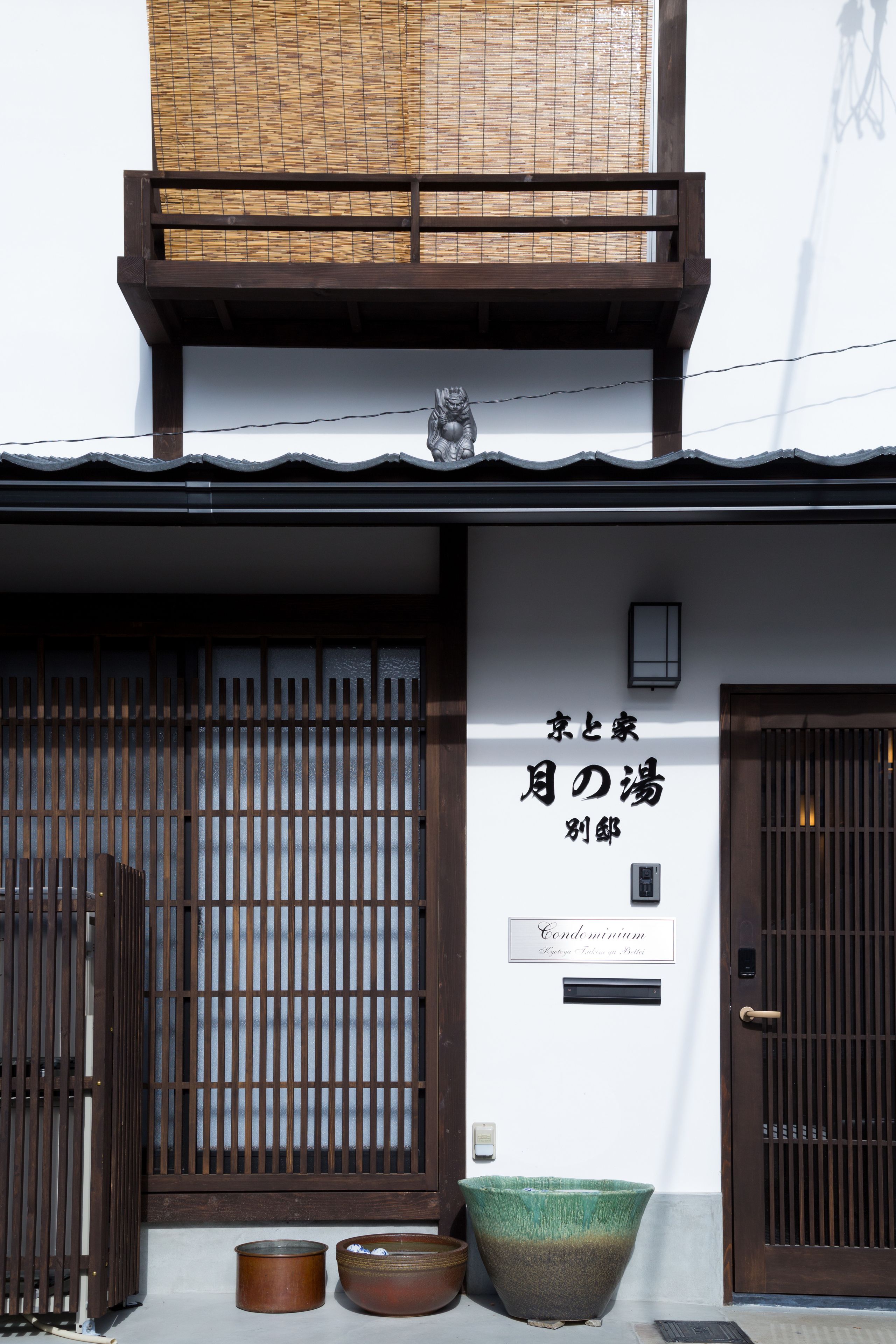 Un bâtiment traditionnel japonais, doté d’une porte en bois, d’un grand pot en céramique et d’une enseigne avec des caractères japonais.