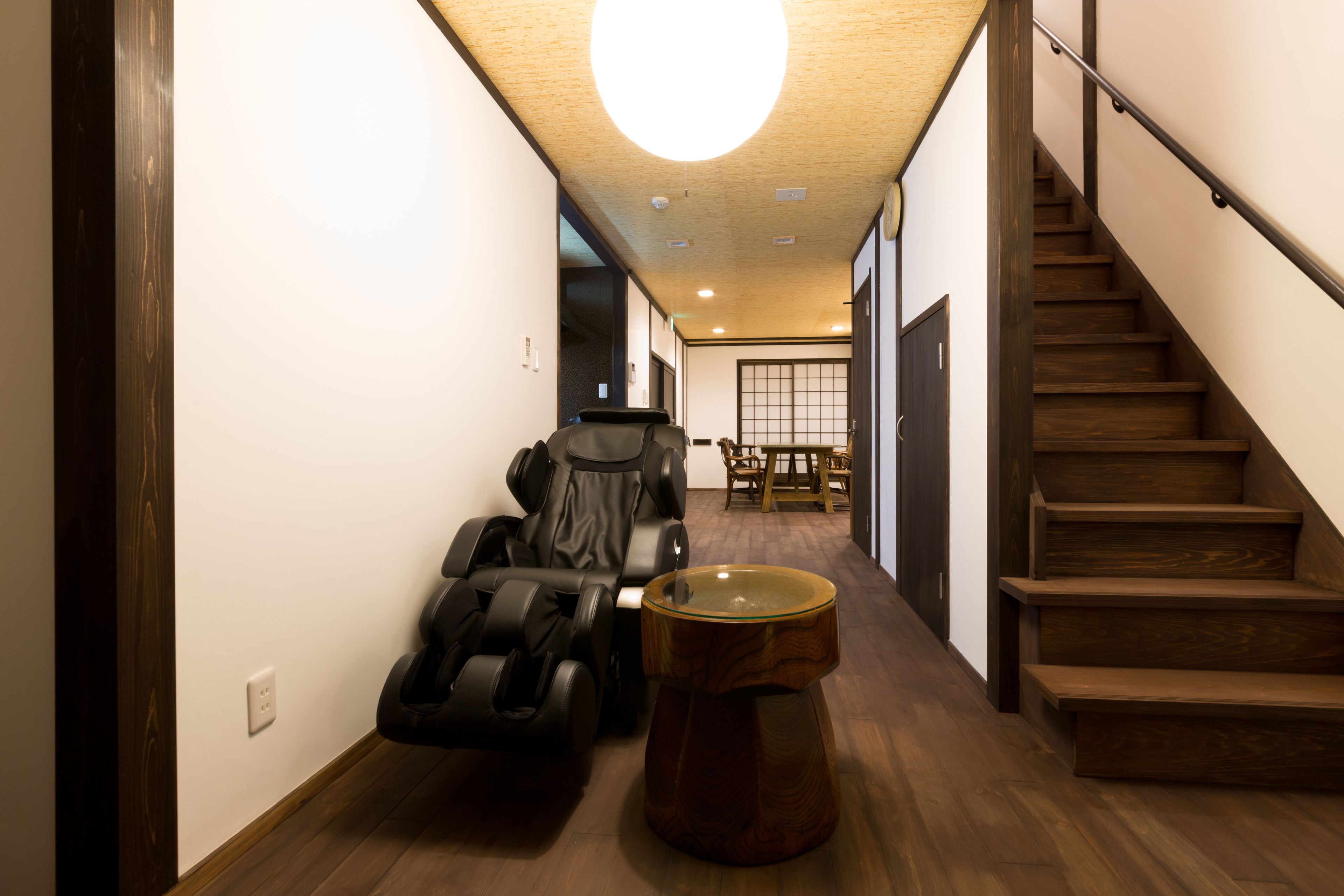Ein Flur mit Massagesessel, Holztisch und einer Treppe.
