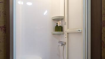A small, enclosed shower area with a toilet, a shelf with toiletries, and a showerhead.
