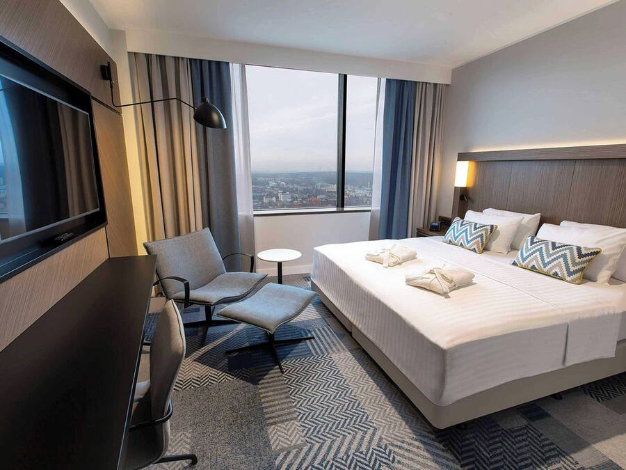 Hotelkamer met een groot bed, een bureau, een stoel, een televisie en uitzicht op de stad.