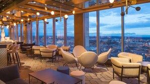 Un intérieur situé dans un immeuble de grande hauteur, offrant une vue panoramique sur la ville, avec des sièges modernes et un espace bar.