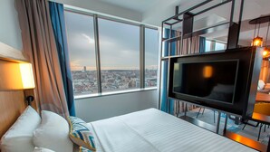 Une chambre d’hôtel avec un grand lit, une télévision et une vue sur la ville par la fenêtre.