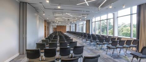 Un salón de conferencias con filas de sillas, ventanas amplias y un diseño moderno en el techo.