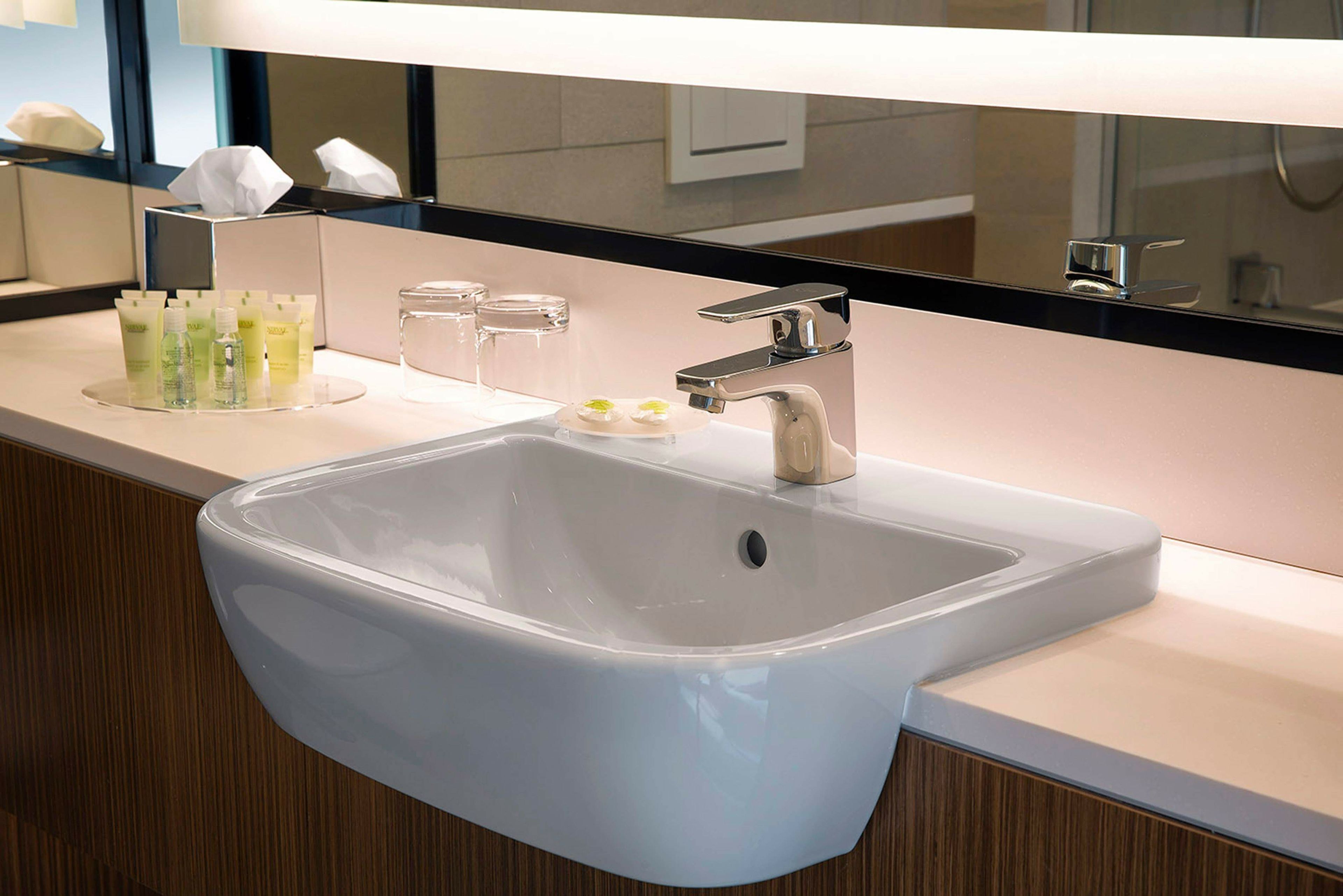 A modern bathroom with a large sink, a mirror above it, and toiletries on the counter.