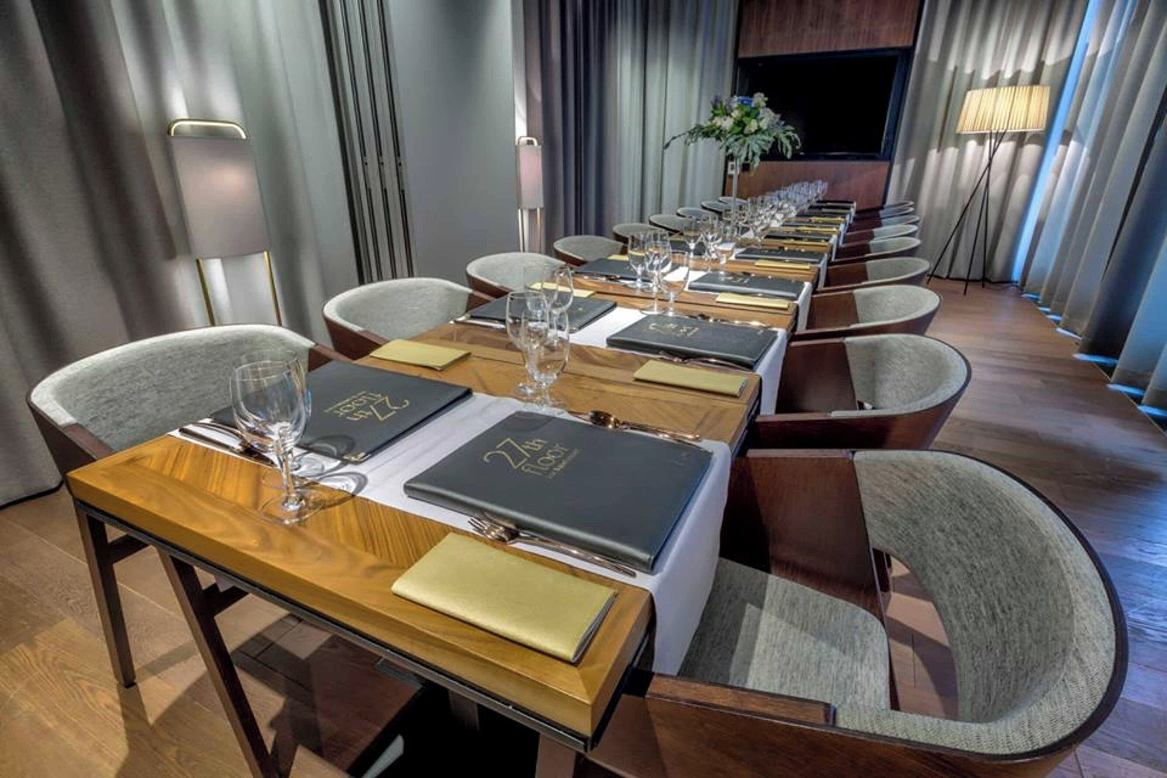 A long dining table set with chairs, menus, and wine glasses, indicating a formal dining area in a hotel.