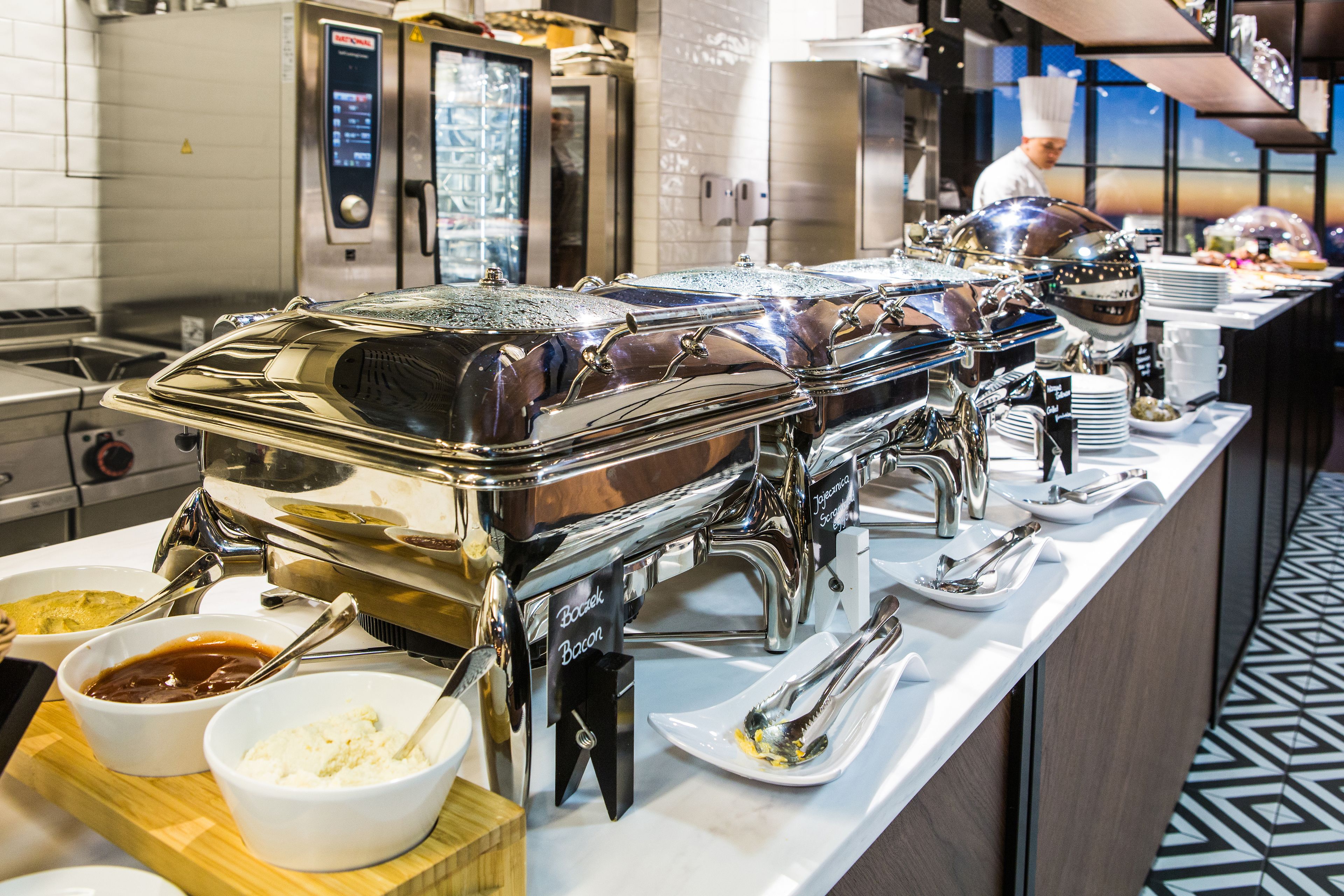 Un buffet avec plusieurs points de service, comprenant des plats de sauces et d’assaisonnements, et un chef cuisinier en arrière-plan.