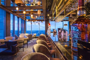 Eine Bar mit einer hohen Theke, verschiedenen Sitzbereichen und Blick auf die Stadt.