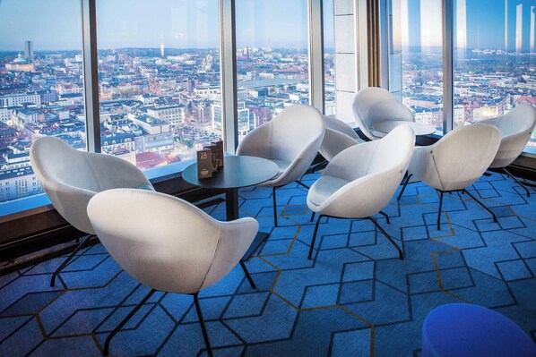 A modern hotel room with a panoramic city view, a round table, and contemporary chairs.