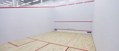 Una cancha de squash con piso de madera y líneas delimitadoras rojas.