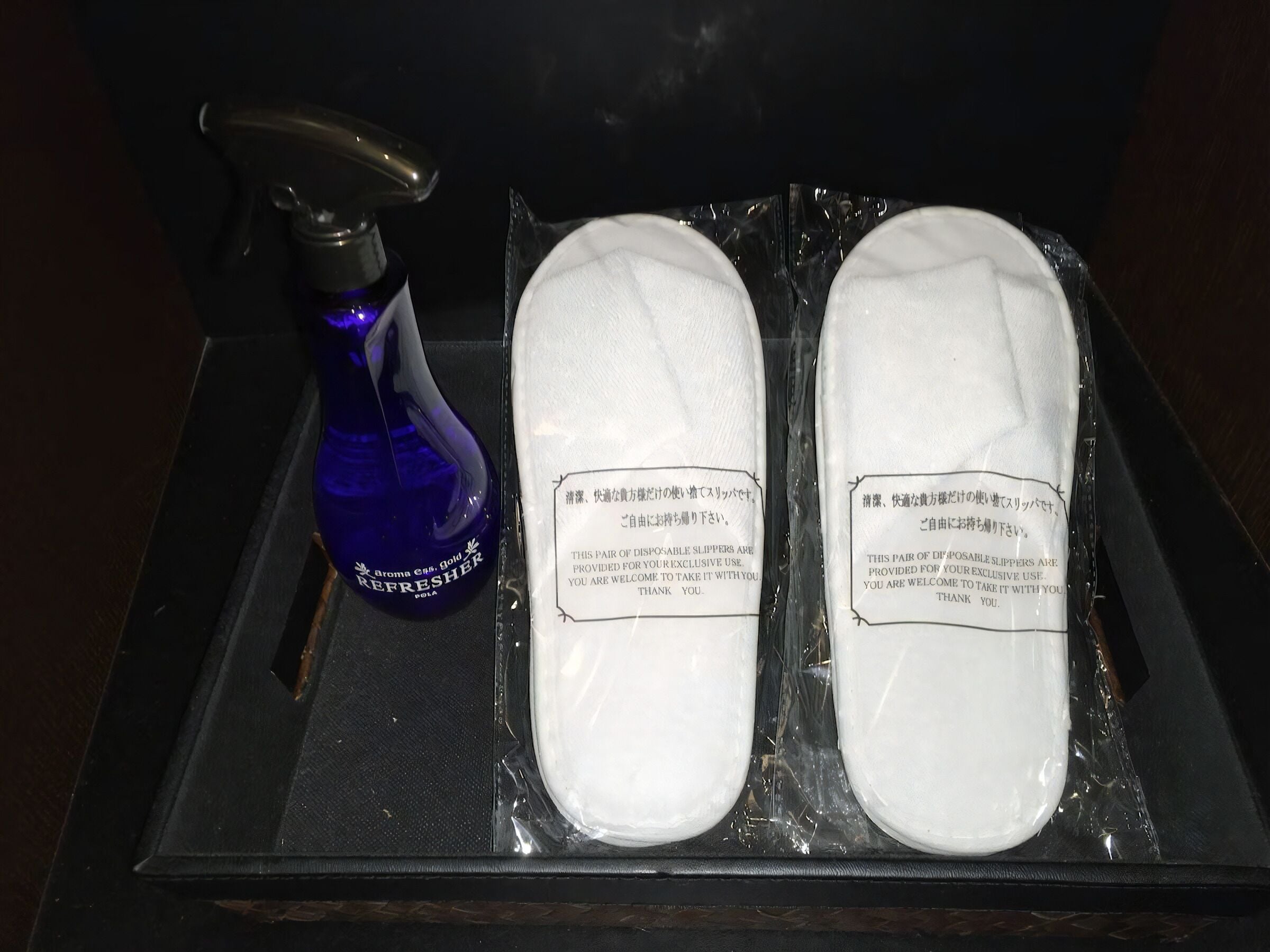Un par de pantuflas desechables y una botella azul rociadora con la etiqueta 'REFRESHER GOLD' sobre una bandeja.