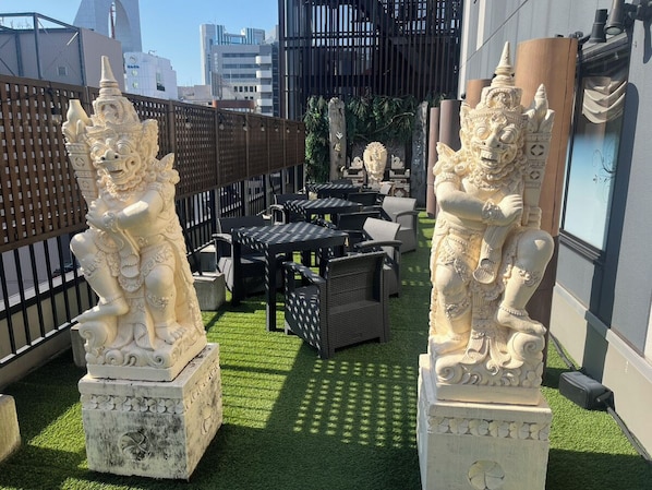 Una terraza en la azotea con dos estatuas de piedra, mobiliario exterior y vistas a la ciudad.