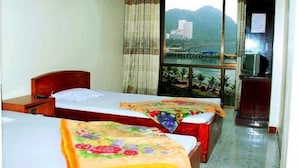 A hotel room with two beds, a wooden headboard, a small desk, and a window with a view of a building and mountains.