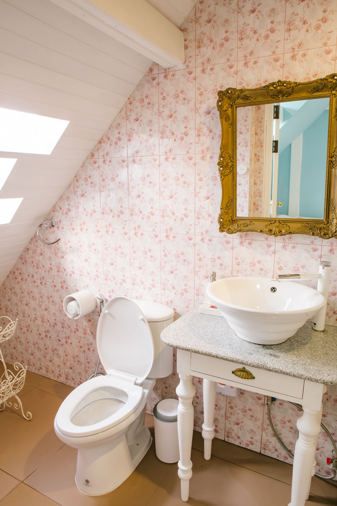A bathroom with a white toilet, a white sink, and a gold-framed mirror.
