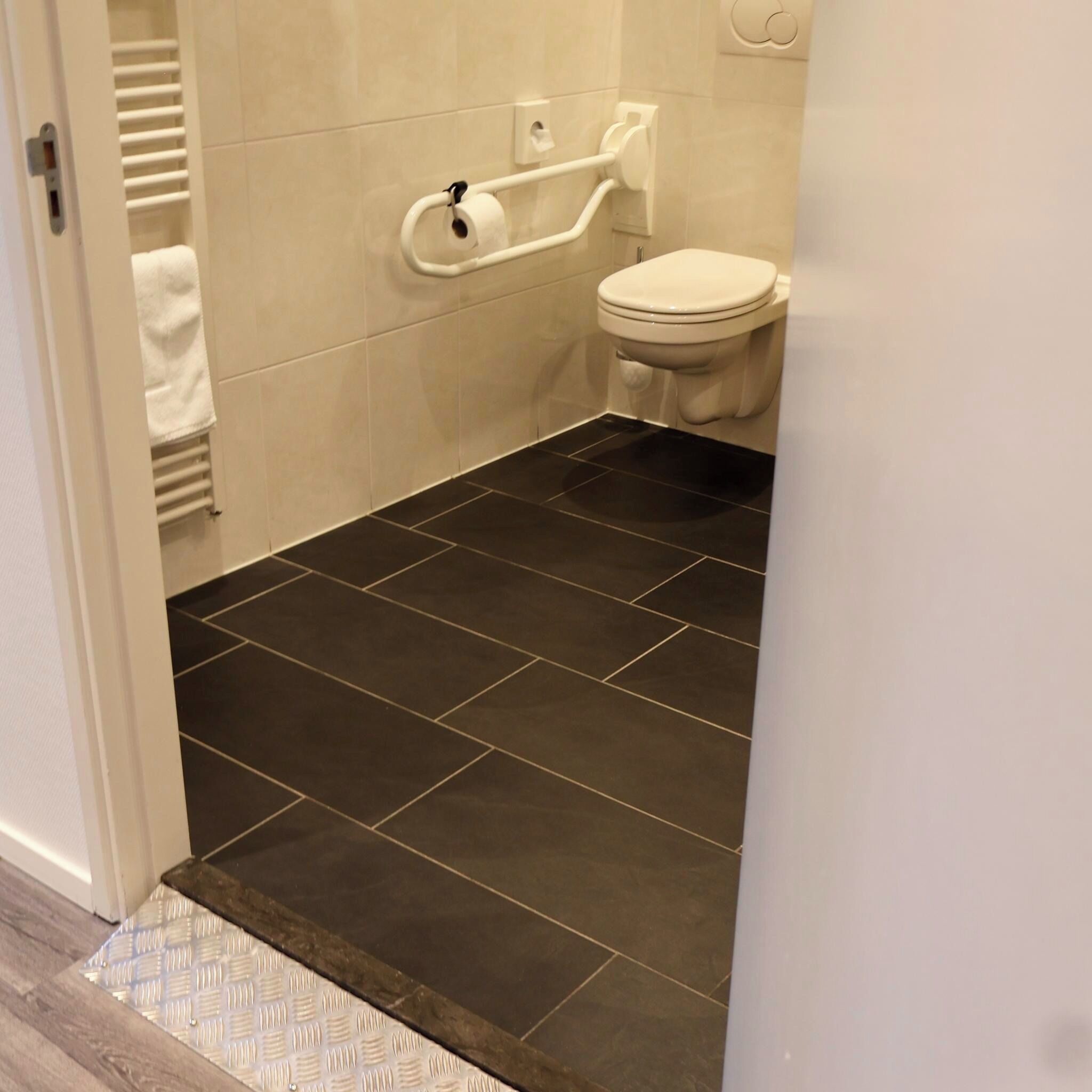 Un bagno con pavimento piastrellato scuro, un water bianco e un porta asciugamani.