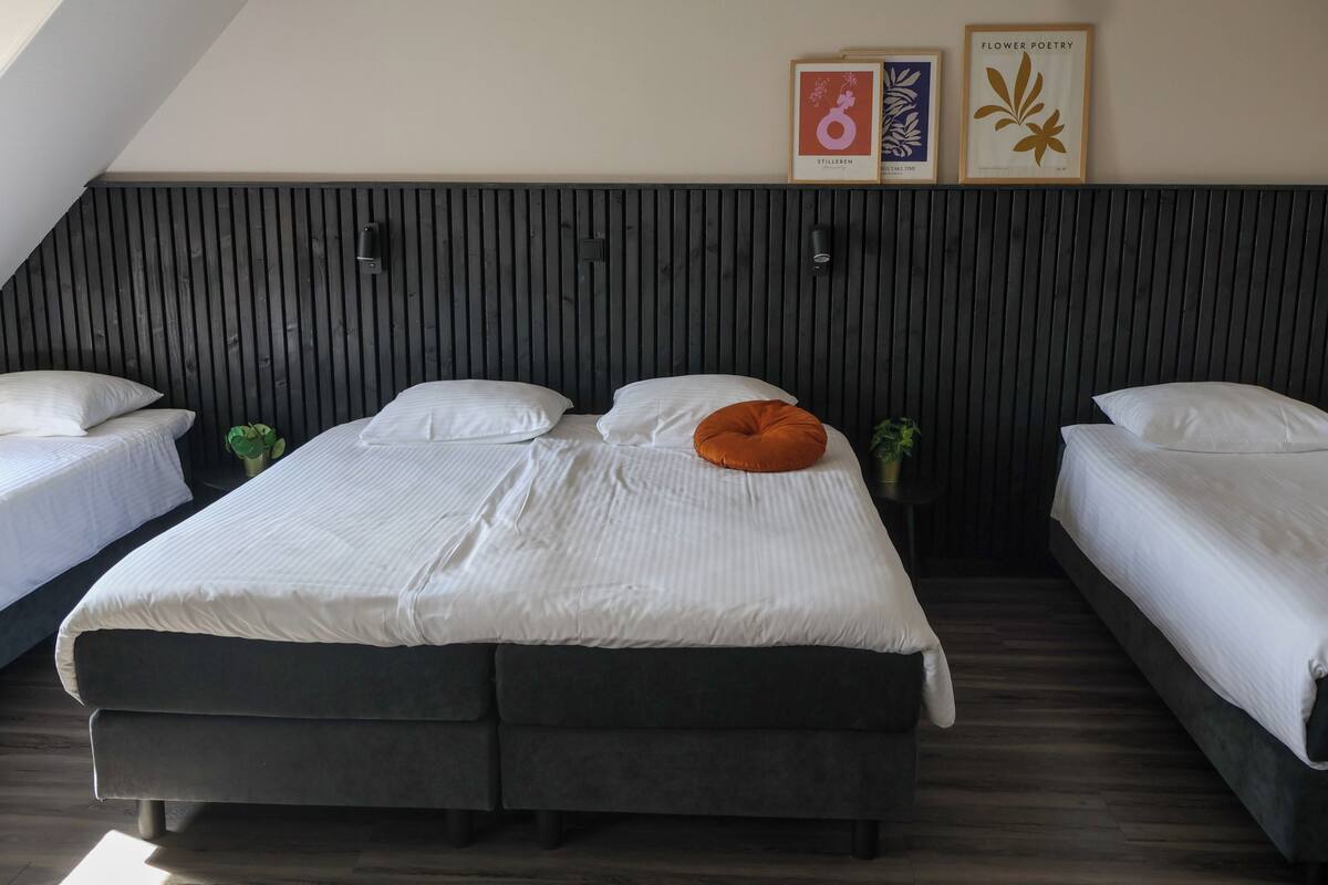 A room with two beds, a wooden slatted headboard, framed artwork, and a small plant.