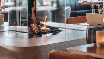 A modern interior with a glass partition, a fire feature, and a wooden table with a book and a glass.