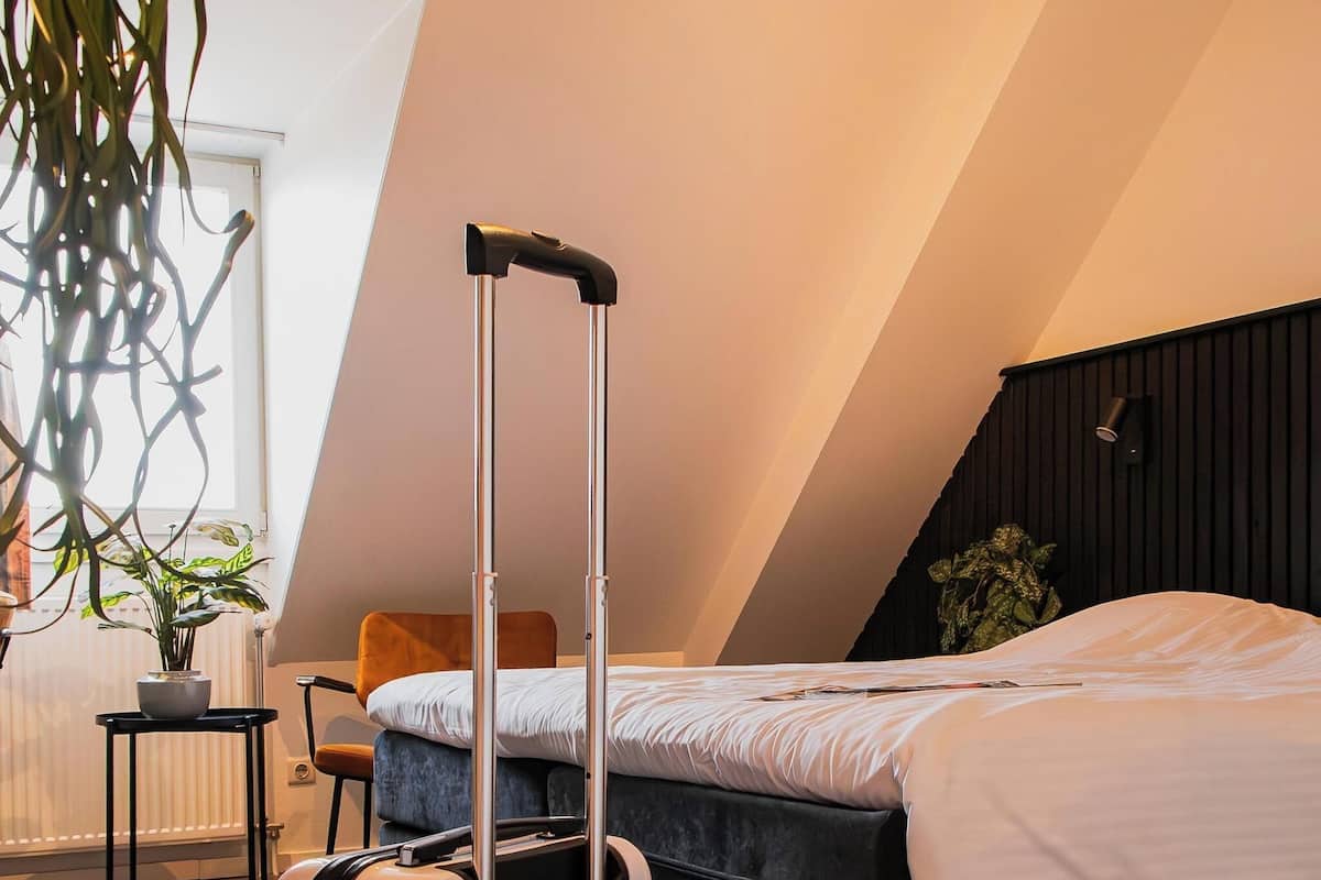 A modern hotel room with a bed, a chair, a small table, and a suitcase.