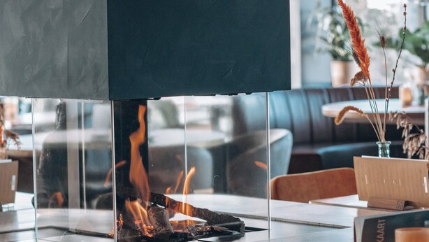 A modern interior with a central fire feature, seating areas, and a visible plant arrangement. - Moeke Mooren (Appeltern)