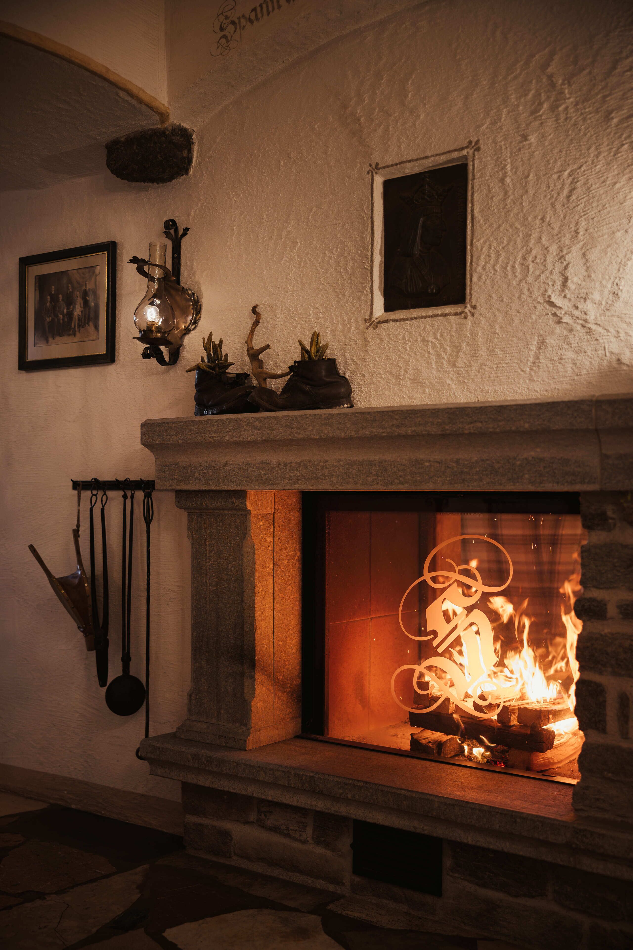 Une cheminée en pierre avec un feu allumé, un tableau encadré au-dessus, et un luminaire fixé au mur sur le côté gauche.