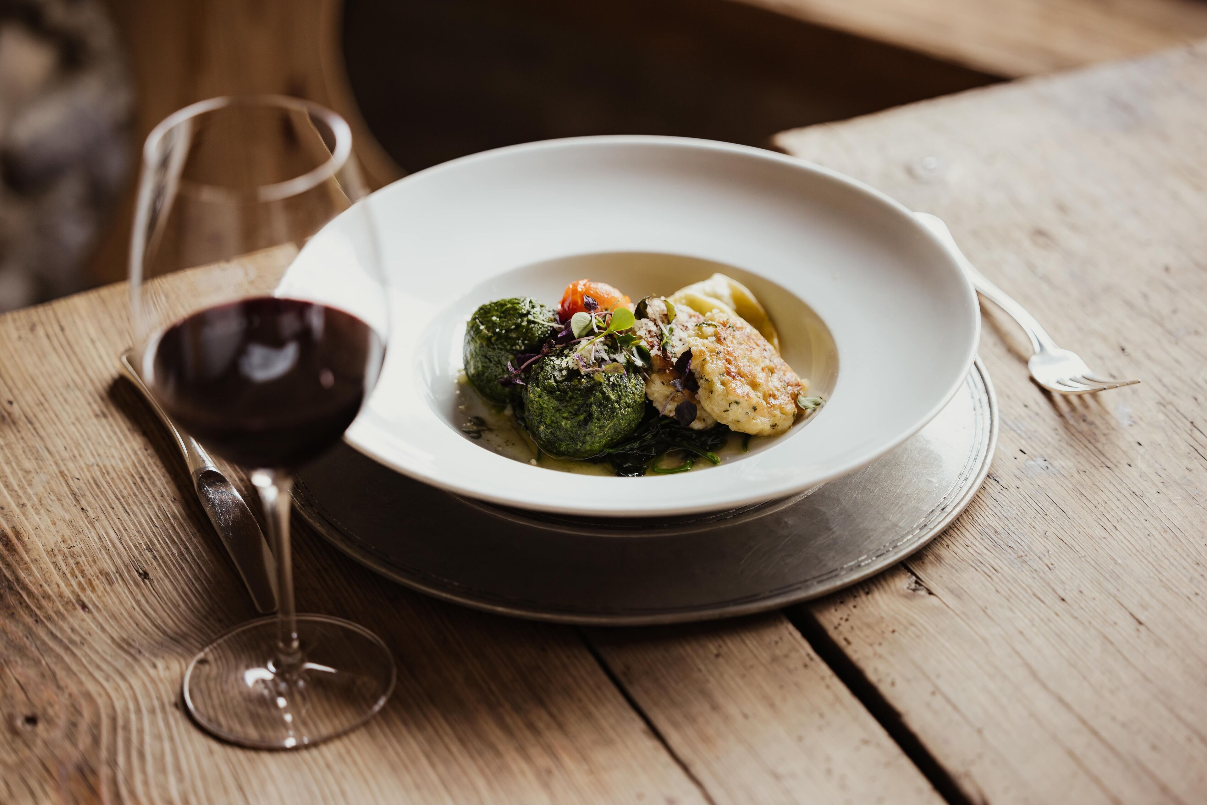 A plate of food on a wooden table with a wine glass.