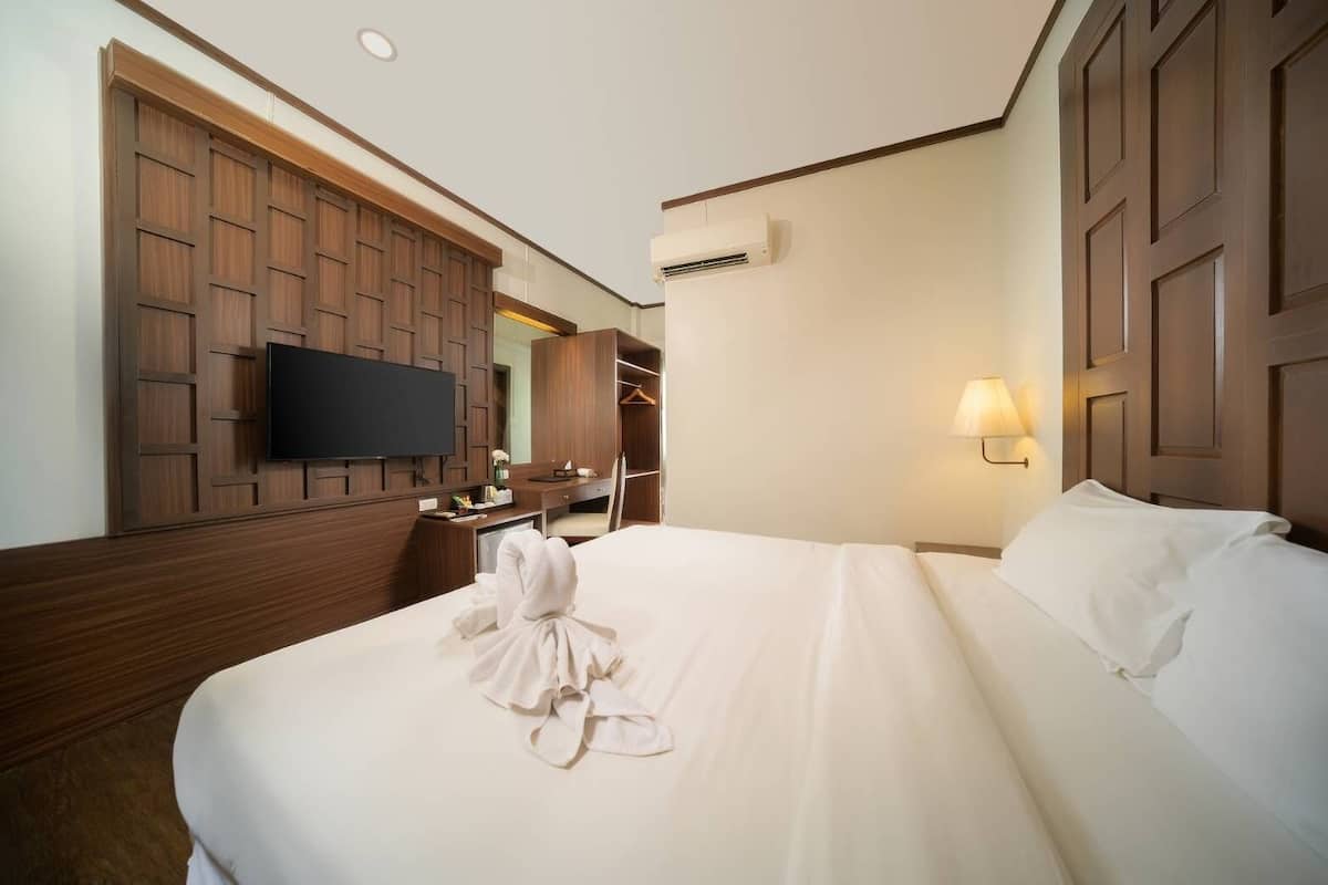 Habitación de hotel con una cama grande, un televisor montado en una pared de paneles de madera, un escritorio con una silla y un armario.