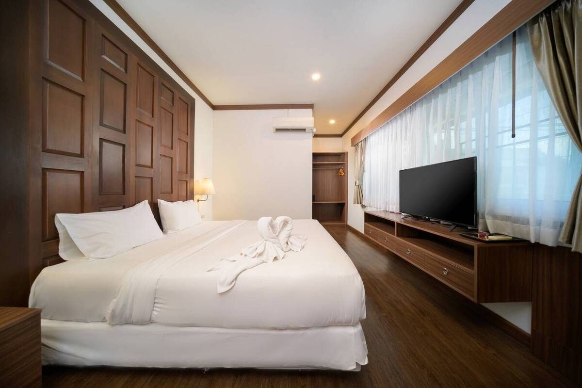 Una habitación de hotel con una cama grande, un televisor sobre un atril de madera y un armario.