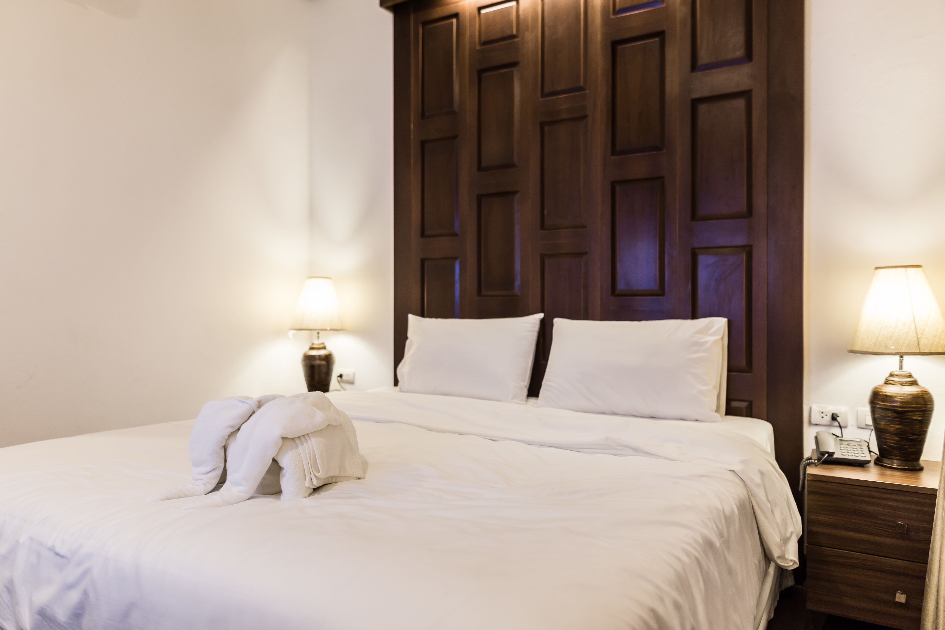 A neatly made bed with white linens, a wooden headboard, and two bedside lamps.